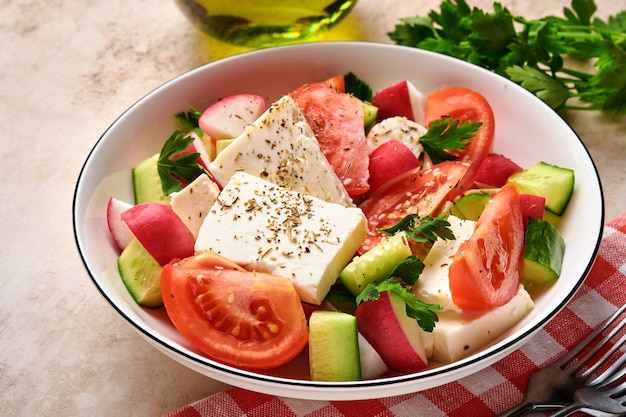 Radis, concombre, tomate, poivre et fromage feta avec épices poivre et huile d'olive dans un bol blanc sur fond gris ardoise, pierre ou béton. Concept d'alimentation saine. Vue de dessus.