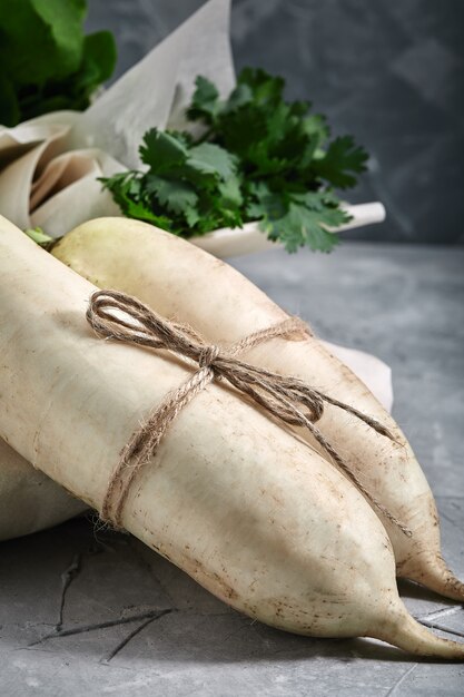 Radis daikon frais sur fond gris, sur fond de grappes de verdure