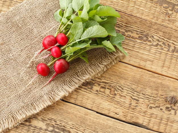 Radis rouges mûrs avec des feuilles vertes sur un sac et des planches de bois