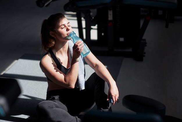 Rafraîchissant avec de l'eau. Photo d'une superbe femme blonde dans la salle de sport pendant son week-end