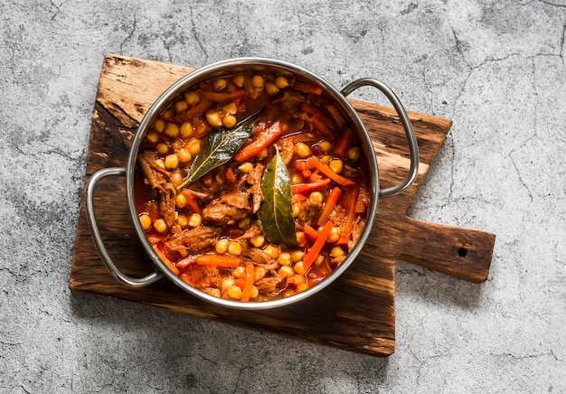 Ragoût de boeuf à la mijoteuse avec des pois chiches dans une casserole sur une vue de dessus de fond gris