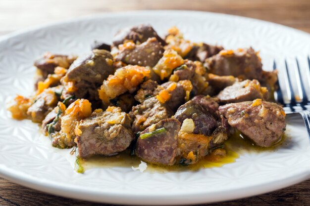 Ragoût de foie de poulet avec des légumes sur une assiette. Fond en bois