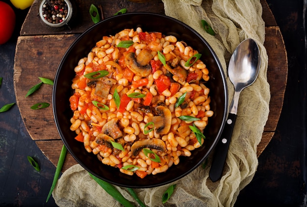 Ragoût de haricots blancs aux champignons et tomates à la sauce épicée dans un bol noir. . Mise à plat