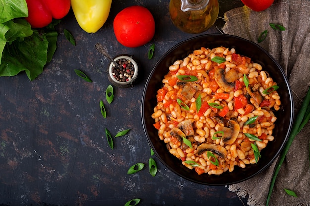 Ragoût de haricots blancs avec champignons et tomates avec sauce épicée dans un bol noir. Vue de dessus Plat poser