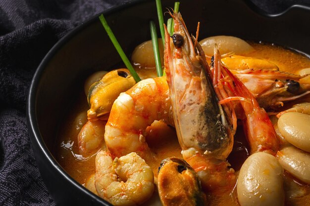 Ragoût de haricots maison avec crevettes et moules sur fond sombre. Cuisine espagnole typique