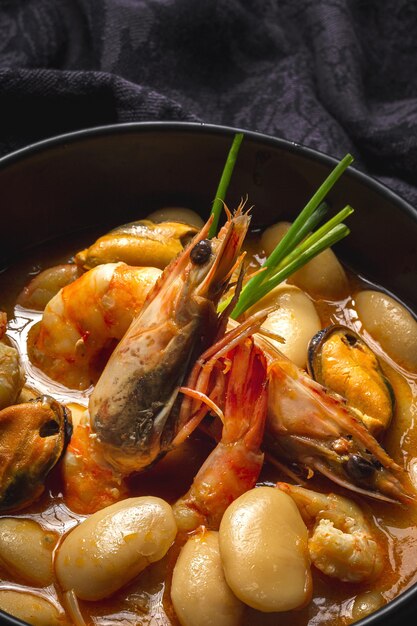 Ragoût de haricots maison avec crevettes et moules sur fond sombre. Cuisine espagnole typique