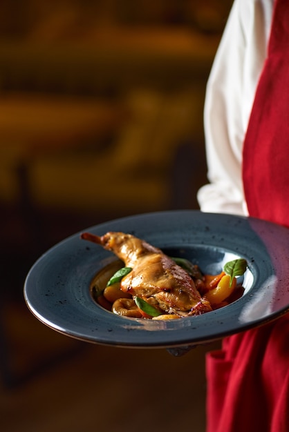 Ragoût de lapin épicé savoureux à la sauce tomate avec du vin blanc et des herbes sur une assiette au restaurant aux mains de la serveuse.