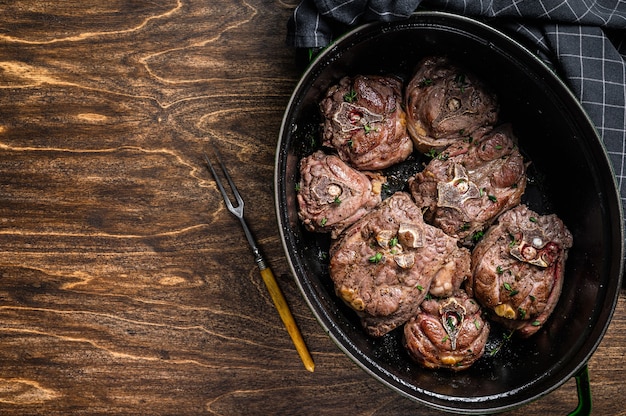 Ragoût de viande de cou d'agneau dans une casserole avec des herbes sur table en bois. Vue de dessus.