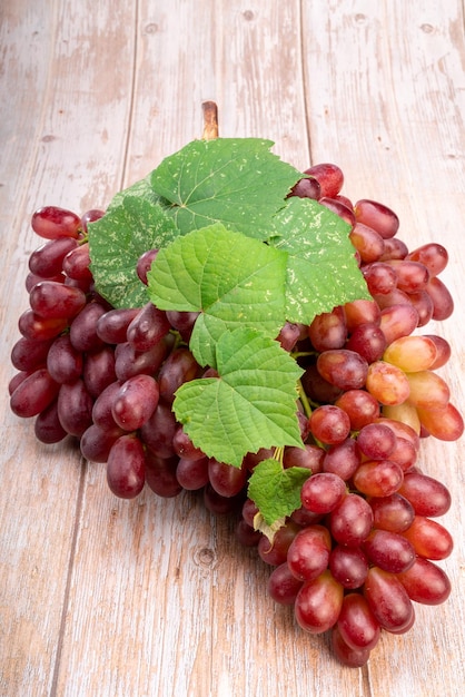 Raisin rouge avec des feuilles sur fond de bois Grappe de raisins rouges frais avec des feuilles