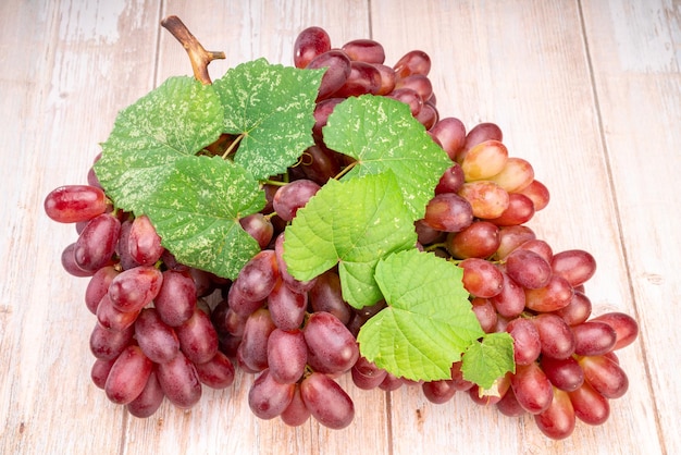 Raisin rouge avec des feuilles sur fond de bois Grappe de raisins rouges frais avec des feuilles