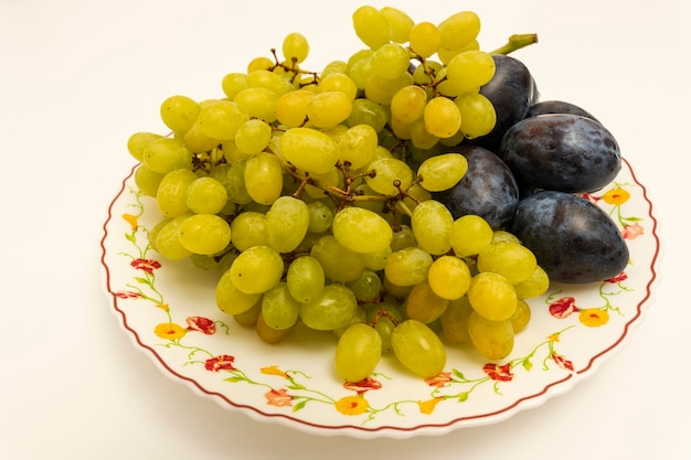 Raisins blancs biologiques mûrs avec des prunes biologiques bleues rondes sur une assiette sur fond rose, fruits, aliments sains, végétarisme. Vue de dessus sous un angle. Nourriture végétalienne