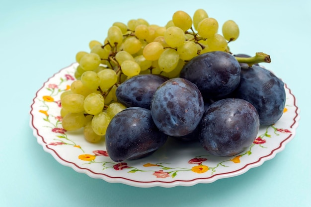 Raisins blancs biologiques mûrs avec des prunes biologiques bleues rondes sur une assiette sur fond turquoise