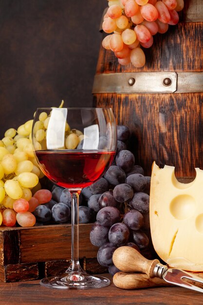 Des raisins, du fromage, un verre de vin rouge et un vieux baril de bois avec un espace de copie.