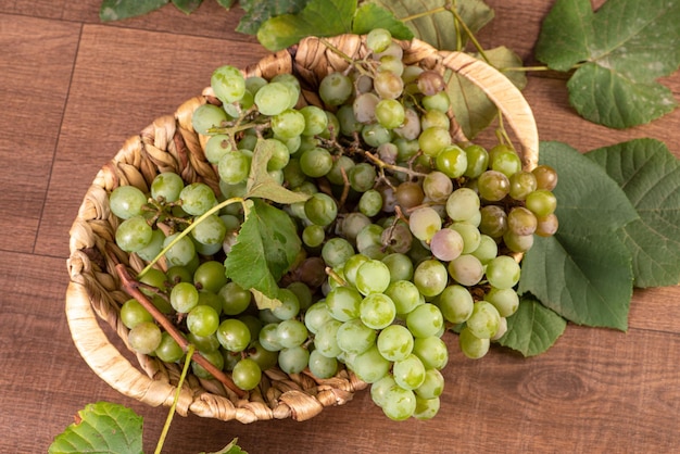 Raisins, grappes de raisins verts placés avec un panier de paille sur une surface en bois, mise au point sélective.