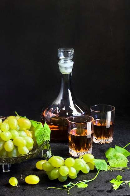 Raisins mûrs frais dans un bol de fruits et une carafe et deux verres de jus de raisin sur fond noir