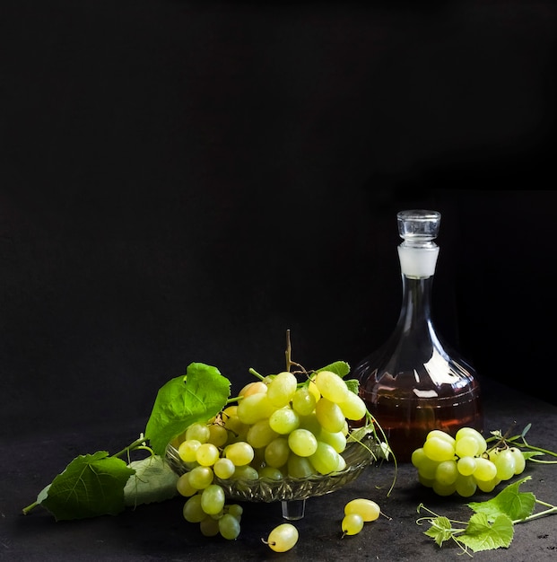 Raisins mûrs frais dans un bol de fruits et carafe avec jus de raisin sur fond noir. Espace de copie