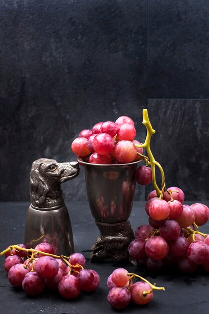 Photo raisins roses dans un verre en métal vintage sur fond noir et une bouteille