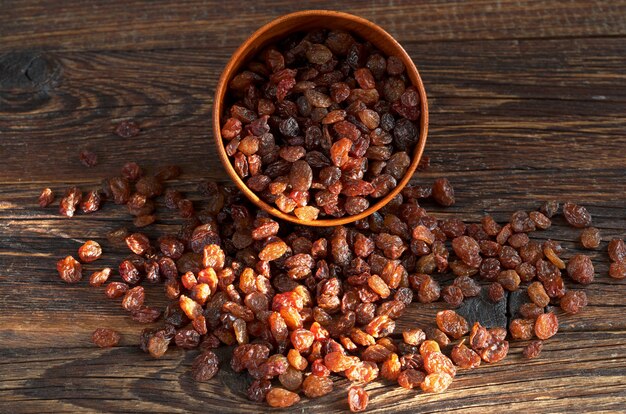 Raisins secs dans un bol et dispersés sur la vieille table en bois