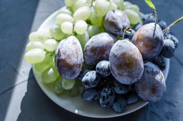 Les raisins sont verts et noirs et une grosse prune sur une assiette blanche