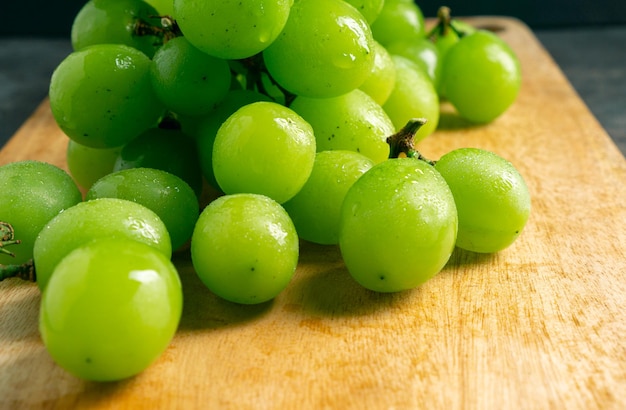 Raisins verts frais sur une planche à découper en bois Prise de vue dans l'obscurité Vue rapprochée Grappe de raisins sur un fond gris en bois Espace pour écrire Convient pour l'été