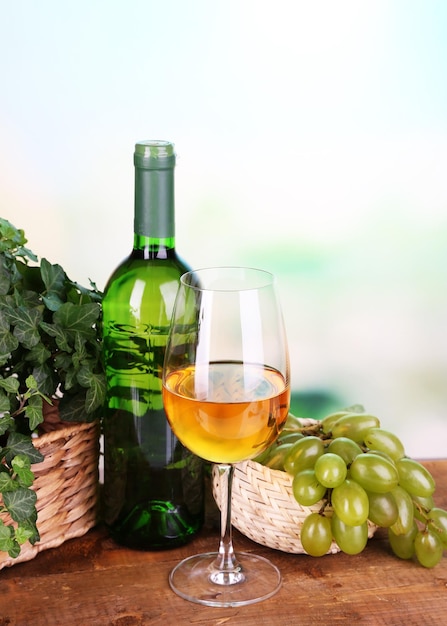 Des raisins verts et violets mûrs dans un panier avec du vin sur une table en bois sur un fond lumineux