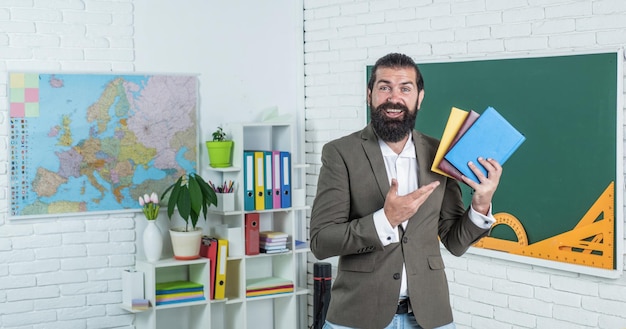 Raison de la formation retour à l'école éducation informelle heureux enseignant mature montrant des livres de la bibliothèque homme barbu travailler en classe avec cahier de travail se préparer à l'examen professeur d'université sur la leçon