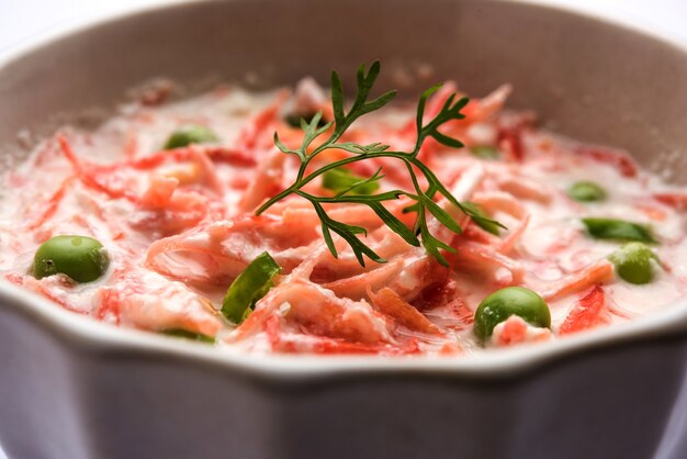 Raïta de carottes OU Gajar Koshimbir avec caillé, vert, pois, piments et coriandre. Servi dans un bol sur fond de mauvaise humeur. mise au point sélective