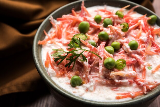 Raïta de carottes OU Gajar Koshimbir avec caillé, vert, pois, piments et coriandre. Servi dans un bol sur fond de mauvaise humeur. mise au point sélective