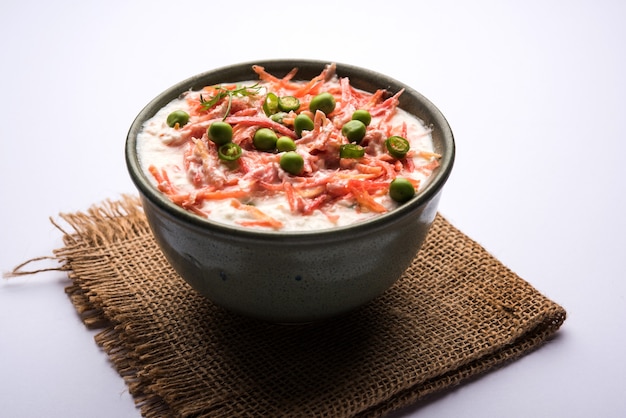 Raïta de carottes OU Gajar Koshimbir avec caillé, vert, pois, piments et coriandre. Servi dans un bol sur fond de mauvaise humeur. mise au point sélective