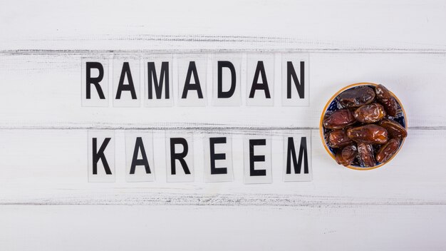 Photo ramadan kareem text avec bol de dattes juteuses sur le bureau blanc
