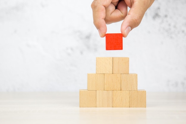 Ramasser à la main des blocs de jouets en bois de cube carré empiler la forme de pyramide sur la table avec un fond blanc de mur pour les activités des enfants