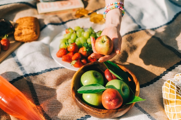 Ramasser à la main une pomme dans un bol en bois avec des fruits frais sur une couverture de pique-nique à l'extérieur