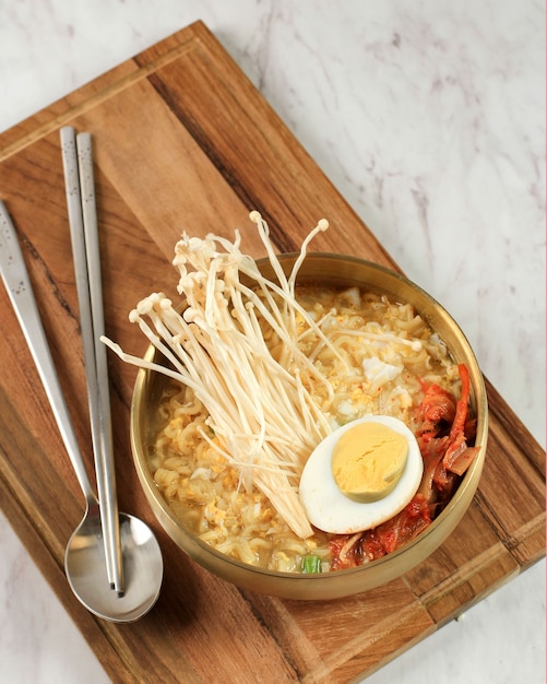 Ramyeon coréen sur bol en or, servir avec des champignons Shimeji, du kimchi et des œufs à moitié durs sur une table en marbre blanc, vue de dessus