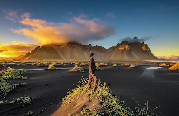 Randonneur appréciant le coucher du soleil à vestrahorn et sa plage de sable noir en islande