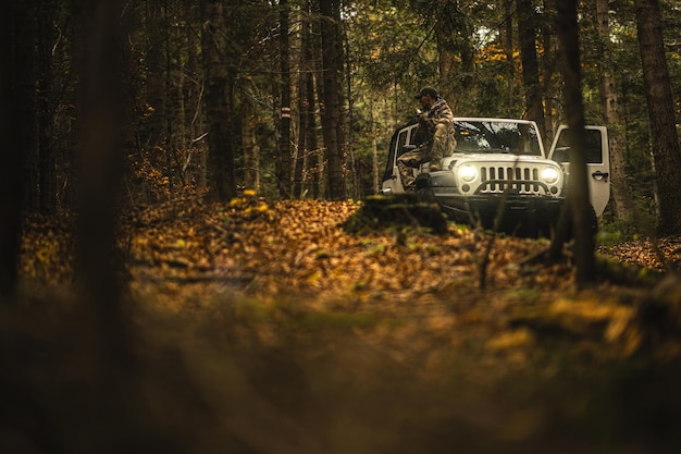 Un randonneur en camouflage apprécie la vue sur la forêt d'automne à côté d'un SUV en fin d'après-midi