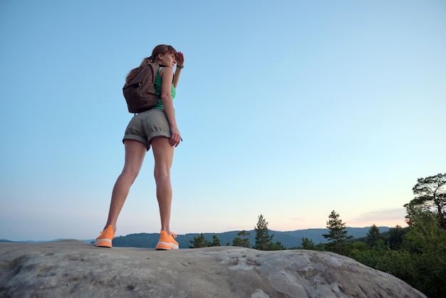 Randonneur femme debout sur un sentier de montagne profitant de la nature du soir pendant son voyage sur un sentier sauvage Voyageur solitaire traversant une route au sommet d'une colline Concept de mode de vie sain