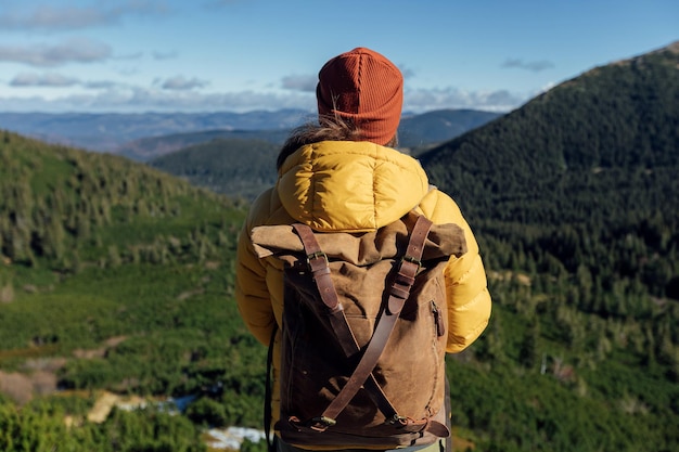 Randonneur femme en veste jaune avec sac à dos de randonnée dans les montagnes de la forêt verte au jour d'automne ensoleillé