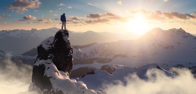 Randonneur homme aventureux debout au sommet d'un pic glacé avec des montagnes rocheuses en arrière-plan