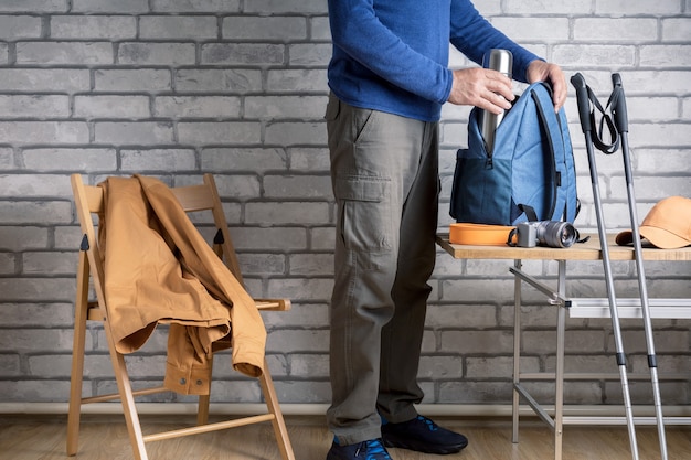 Randonneur Homme Debout Avec Des Choses De Randonnée Disposées Sur Une Table à La Maison Ou à L'hôtel. Concept De Voyage, D'aventure, De Mode De Vie Actif.