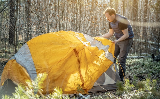 Un randonneur installe une tente orange vif dans la forêt. Concept de tourisme, de randonnée et de séjour dans la nature.