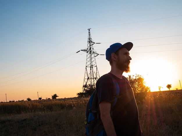 Randonneur avec sac à dos debout sur une colline et profitant du coucher du soleil Homme barbu en snapback marchant Concept nature voyage local