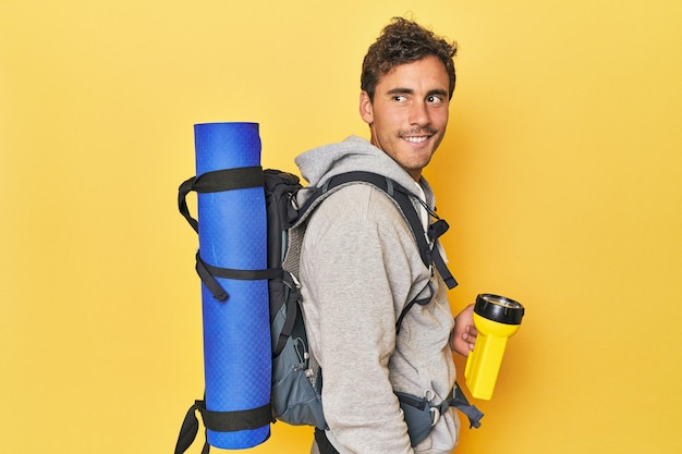 Randonneur avec sac à dos et lanterne sur jaune regarde de côté souriant joyeux et agréable