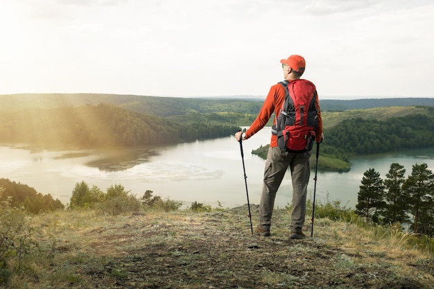 Un randonneur avec un sac à dos se détend au sommet d'une colline et profite de la vue sur la vallée avec les montagnes et le lac