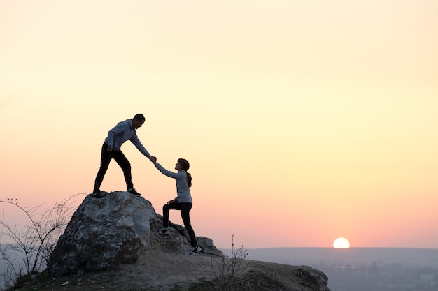 Randonneurs homme et femme s'entraident pour grimper la pierre au coucher du soleil dans les montagnes