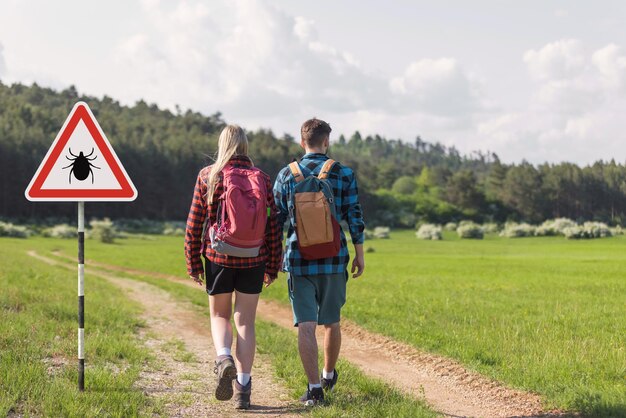 Randonneurs passant devant une zone infectée par des tiques avec un signe de danger, risque de transmission par les tiques et de maladie de Lyme