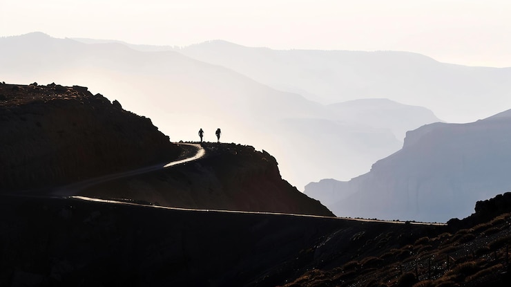 Photo des randonneurs en silhouette sur un sentier de montagne sinueux à travers un paysage accidenté avec une vue spectaculaire
