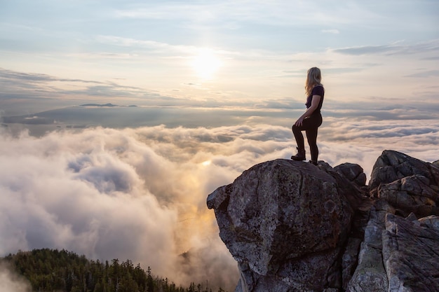 Randonneuse aventureuse au sommet d'une montagne couverte de nuages pendant un coucher de soleil d'été animé