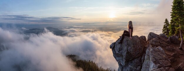 Randonneuse aventureuse au sommet d'une montagne couverte de nuages pendant un coucher de soleil d'été animé