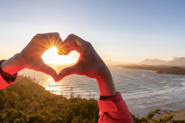 Randonneuse aventureuse en forme de coeur avec les mains sur une plage de sable sur la côte ouest