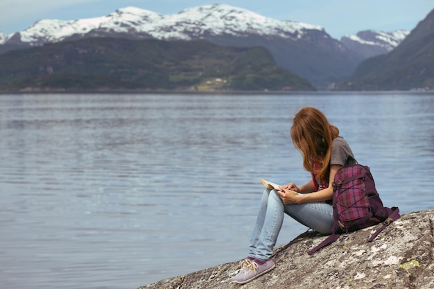 Randonneuse de fille avec un livre se reposant sur un rocher sur un fond de montagnes et de lacs, norvège